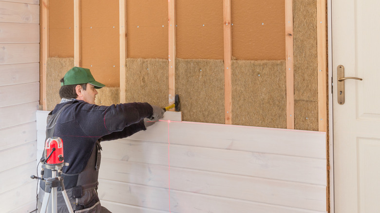 Worker installing natural fiber insulation and wood panel to a half-built wall frame