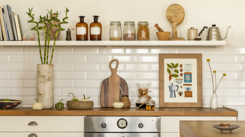 A white tile kitchen backsplash lined with rustic accessories on a wood counter and a painting.