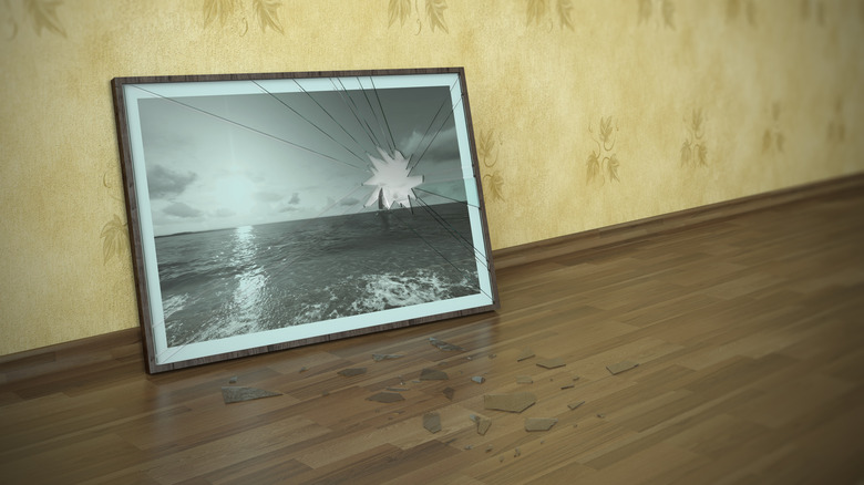 A broken picture frame and broken glass lying on the floor near a wall.