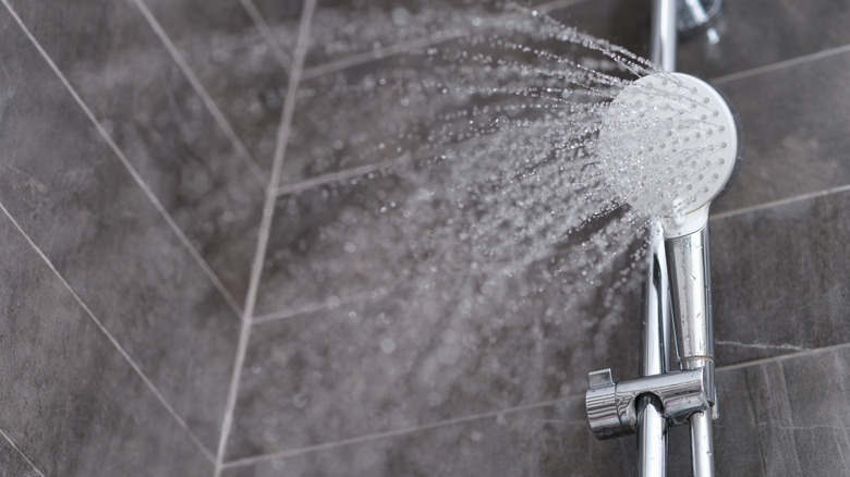 Water spraying from a showerhead against dark tiles