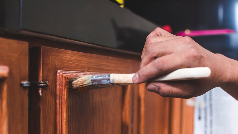 Person with paintbrush varnishing cabinet