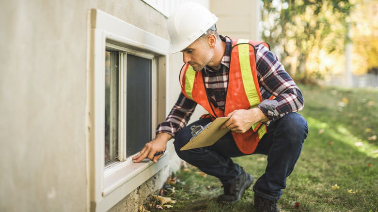 A home inspector holds a clipboard while examining an outdoor window
