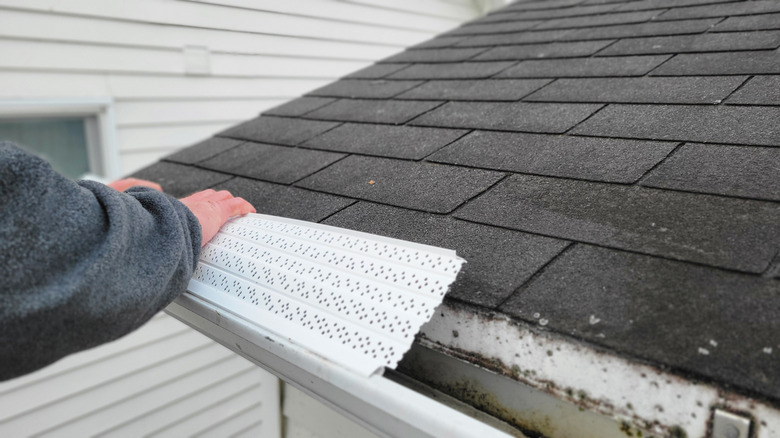 Person installing white plastic gutter cover