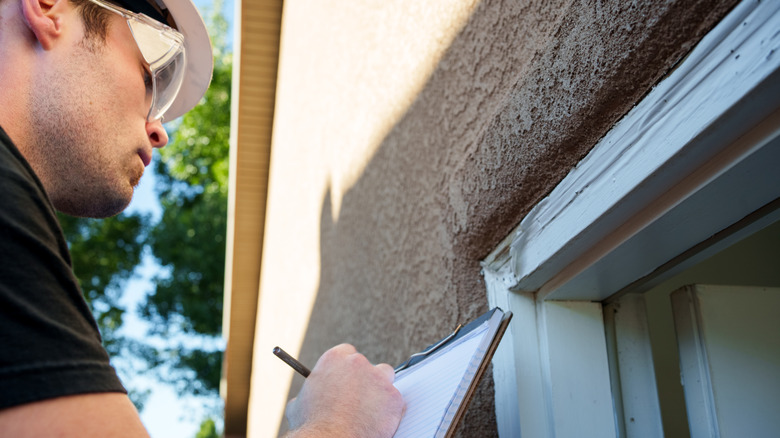 Someone inspecting the exterior of a stucco house.