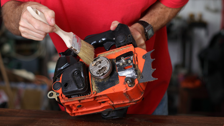 A man brushing down the internal components of a chainsaw with the sprocket cover, bar, and chain removed