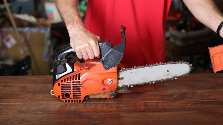 Close-up of a man preparing to clean and maintain a chainsaw on a wooden counter