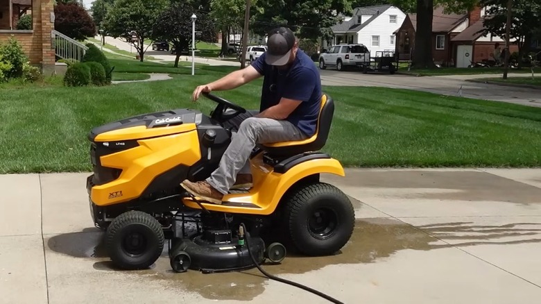 Man cleaning a riding mower deck with the hose attachment