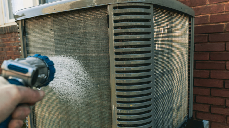 A man spraying an air conditioner with a hose