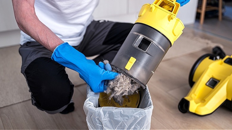 Close-up of a person wearing blue gloves, emptying vacuum canister into trash