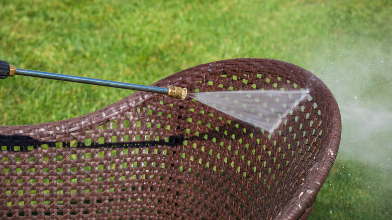 A brown wicker chair being sprayed with a pressure washer