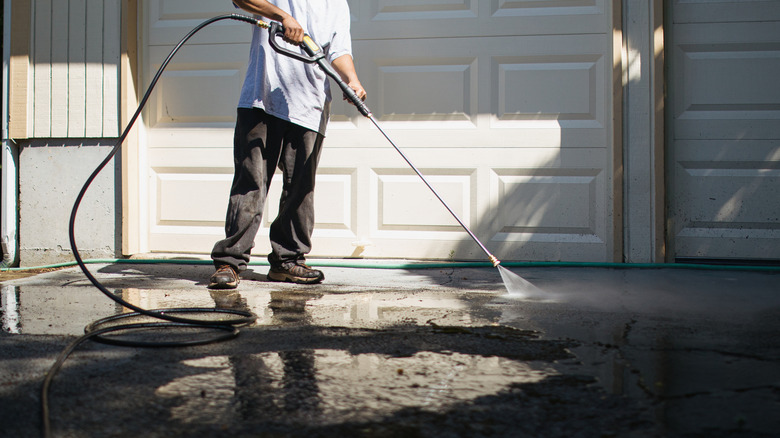 A person using a pressure washer outside of their garage