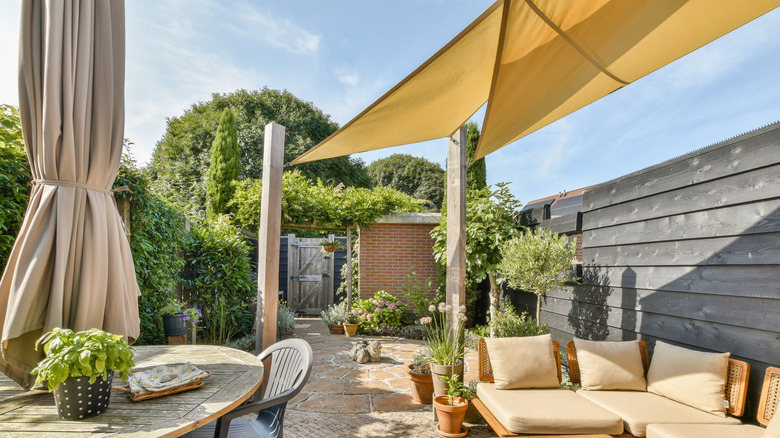 A beautifully arranged outdoor garden patio featuring comfortable seating, vibrant greenery, and a stylish shade sail.