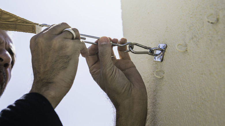 Man installing a sail shade on a building's terrace.