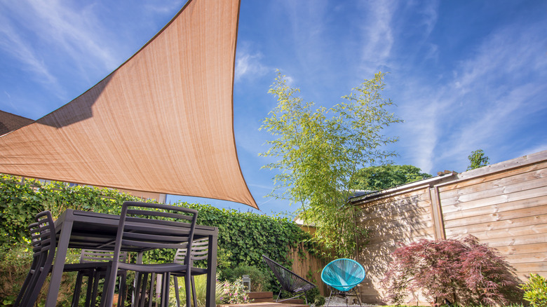 Modern house terrace in summer with table and shade sail.