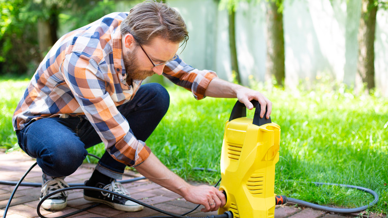 Man using pressure washer on brick walkway