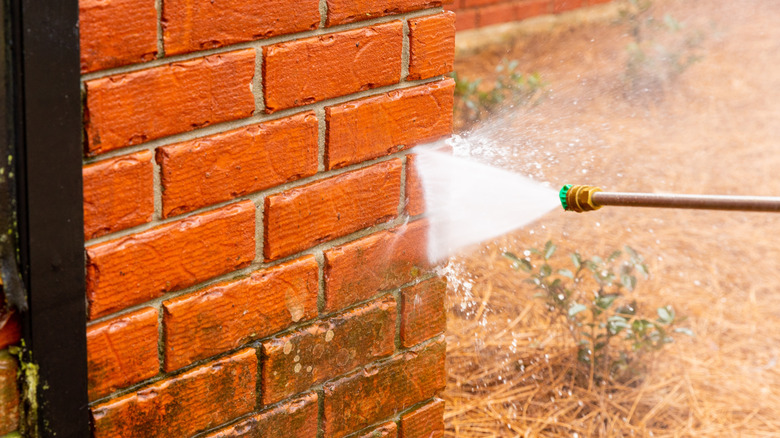 Pressure washer using water to clean a dirty brick wall on a house.