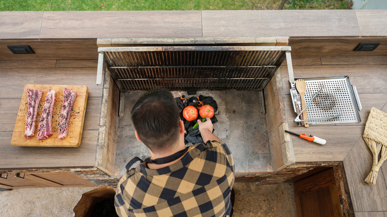 A man using a wind blocker to cook on a grill.