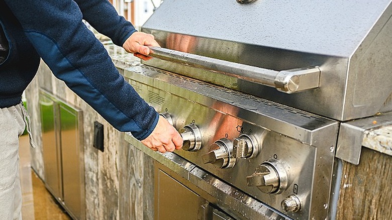 Person turning knobs on a stainless steel grill in an outdoor kitchen area