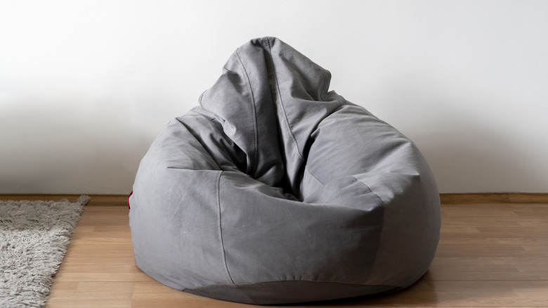 A gray bean bag chair on a wooden floor next to a gray rug