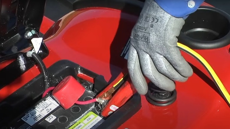 Person hooking jumper cables to a lawn mower battery