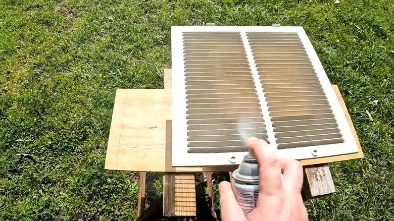Person spray painting a white air vent outdoors