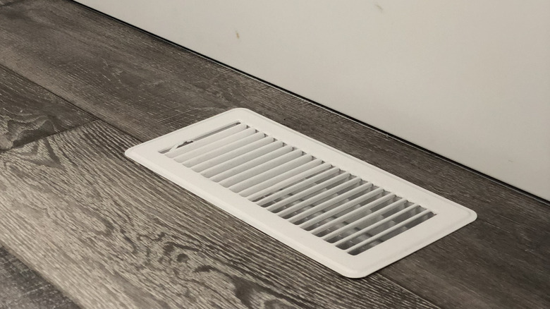 A white air vent in a grey wood floor