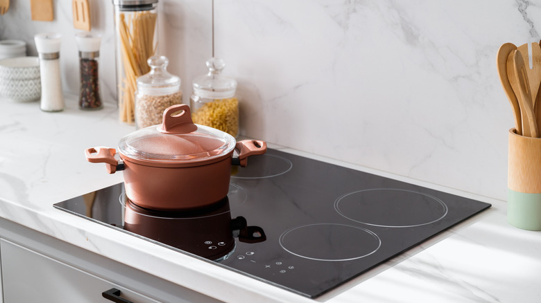 A stylish saucepan on top of a clean new and black induction stove on marble countertop in a white kitchen.