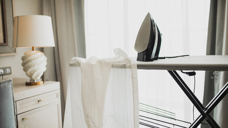 Iron sitting up on an ironing board with a shirt hanging off the board