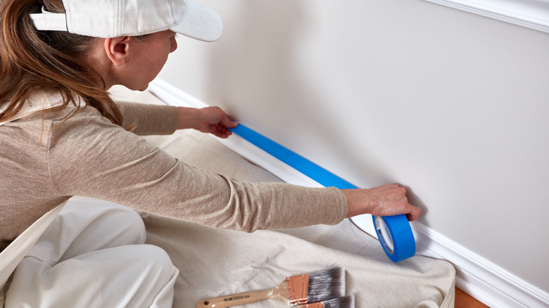 Woman preps baseboard for paint