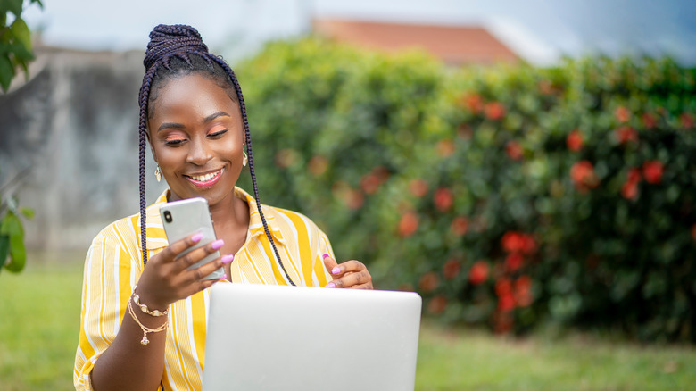 African American woman using smartphone and laptop in garden