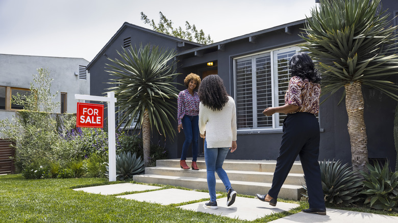 Two people and a realtor stand outside a house with a for sale sign
