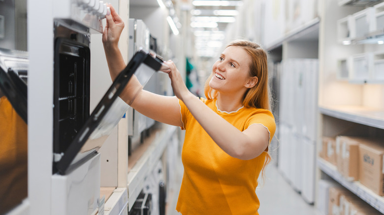 A woman smiles as she opens a new electric oven for the kitchen in a store.