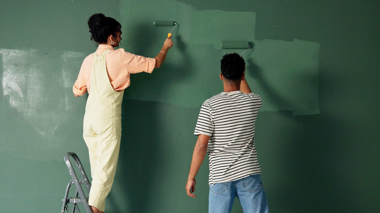 A couple paints a dark green wall using rollers