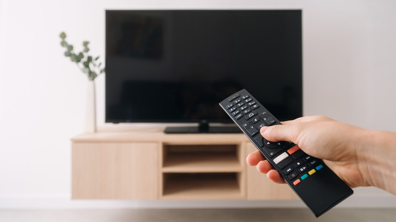 Hand pointing a remote to a powered-off TV on a floating wall cabinet