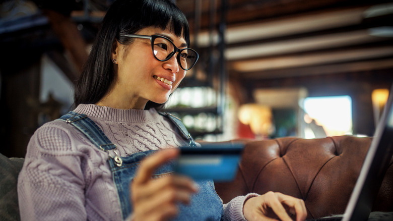 A woman holds her credit card while shopping on her laptop.