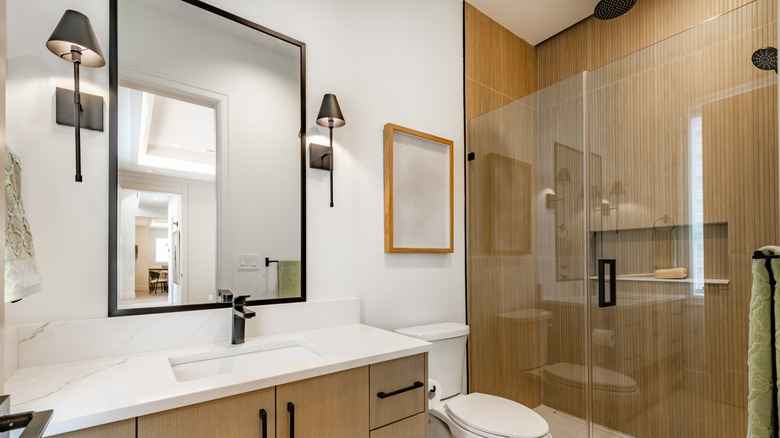 Modern bathroom with black framed mirror flanked by sconces