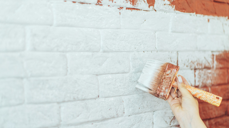 Closeup of a woman's hand painting a brick wall white
