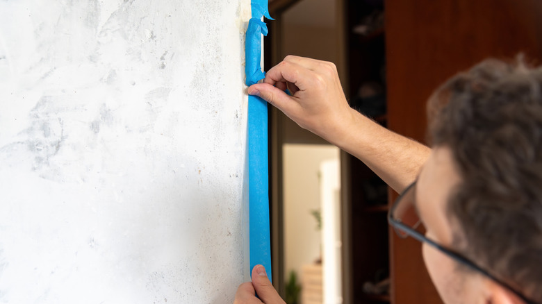 Man applying painter's tape along wall