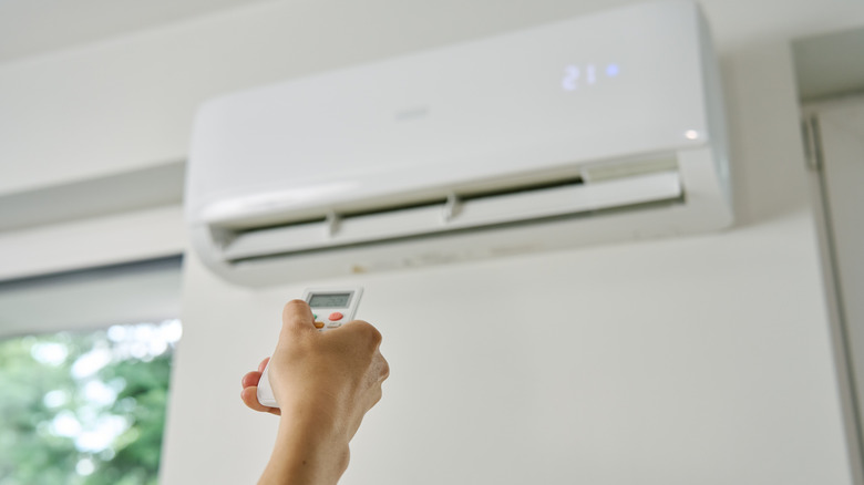 A hand holding a remote to turn on a white wall unit air conditioner