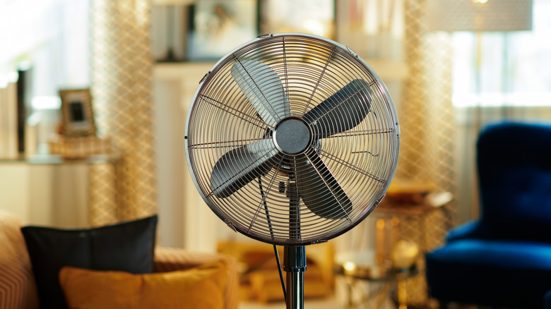 A metal standing fan in the middle of a blue and gold living room