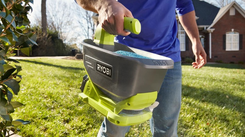 A person spreading material onto lawn with a Ryobi hand spreader