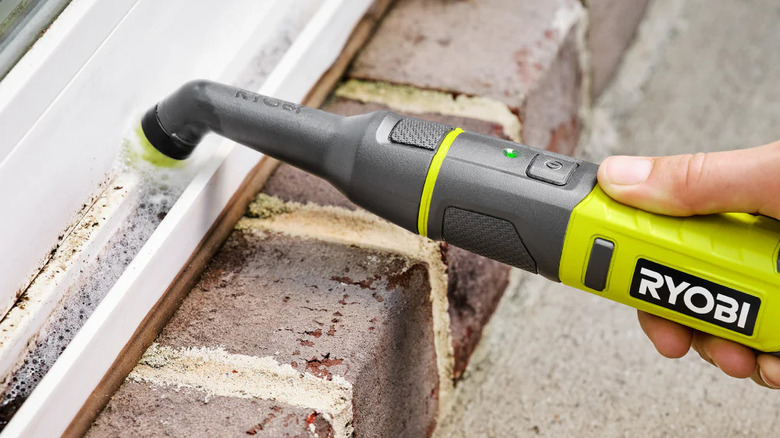 A person uses the Ryobi USB Lithium Cordless Compast Detail Scrubber to clean a window sill