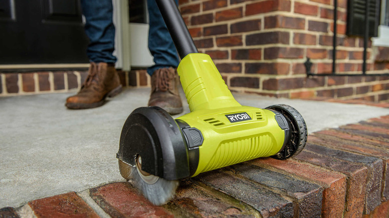 A man uses a Ryobi Cordless Outdoor Patio Cleaner to scrub algae off a brick patio