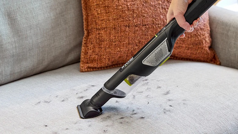 A person vacuuming hair off of a couch with a Ryobi USB compact hand vacuum