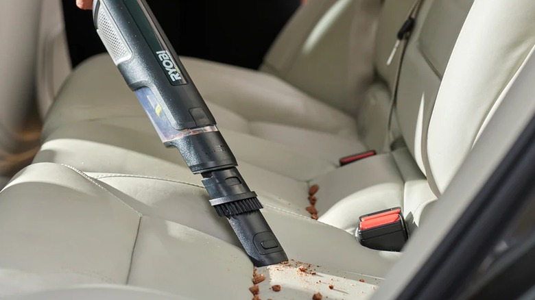 A person using a Ryobi USB compact hand vacuum to vacuum crumbs off of a car seat