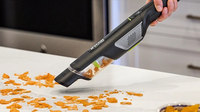 A person cleaning crumbs off of a counter with a Ryobi USB compact hand vacuum