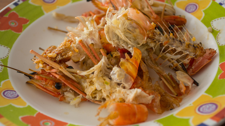 A plate full of seafood leftovers including shells, heads, and fish bones.