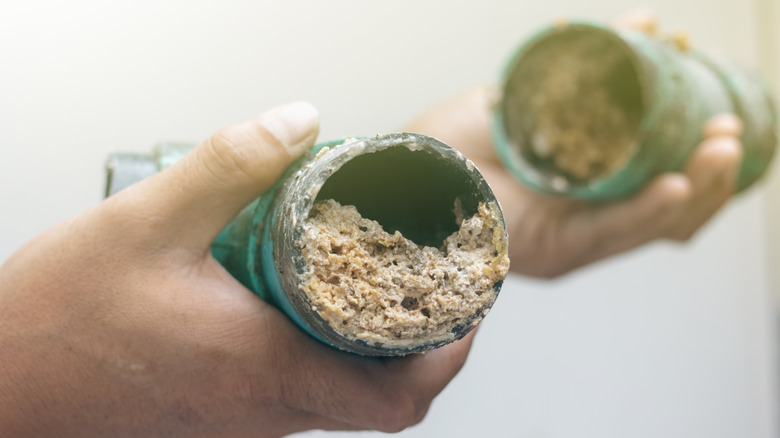 A person holds a drain pipe clogged with solidified grease and debris