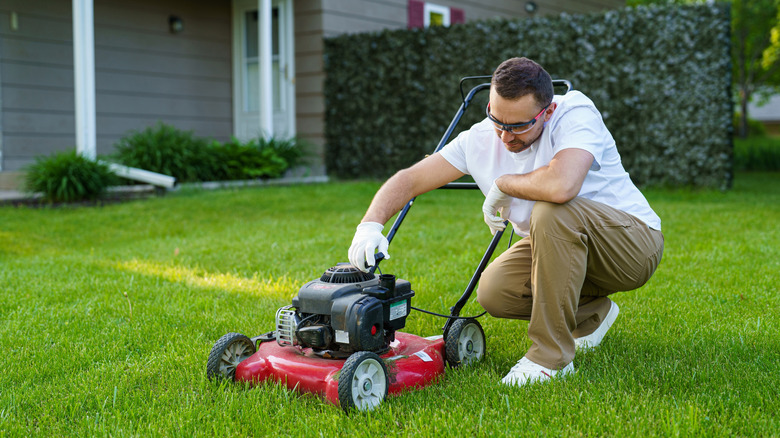 A man squatting to adjust a red lawn mower
