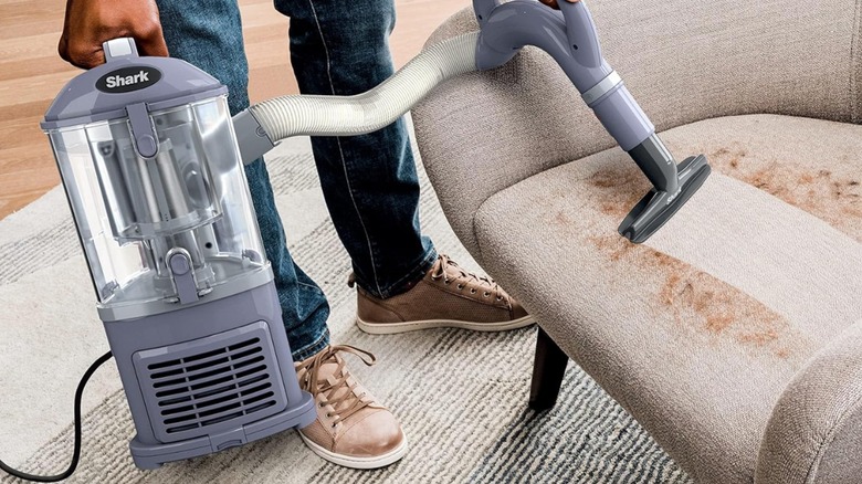person using attachments to vacuum pet hair off chair